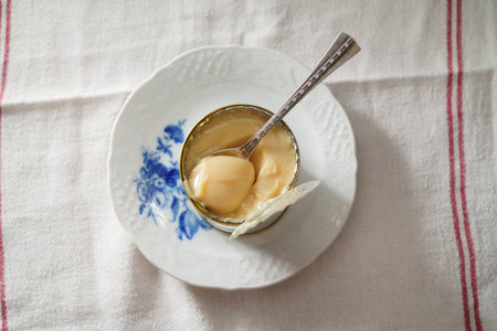 Condensed milk in a tin can on a white plate. Dulce de leche with metal spoon. Vintage style.の写真素材