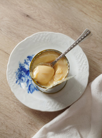 Condensed milk in a tin can on wooden table. Dulce de leche with metal spoon. Vintage style.の写真素材