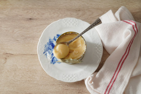 Condensed milk in a tin can on wooden table. Dulce de leche with metal spoon. Vintage style.の写真素材