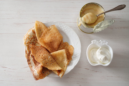 Homemade crepes on white background with condensed milk in tin tan and sour cream. Top view.の写真素材