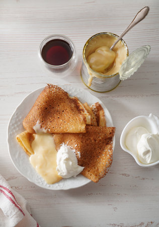 Homemade crepes on white background with condensed milk in tin tan and sour cream. Top view.の写真素材