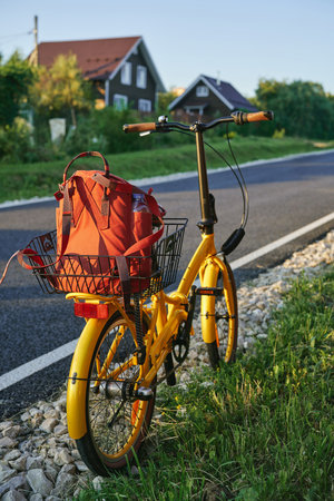 Yellow bicycle standing on the side of a rural road. Red backpack on the trunk of bicycle. There are beautiful village houses in the background.の写真素材