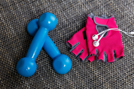 Fitness gym equipment. Workout gloves and blue dumbbells. Sport accessories. White headphones for music and mood.の写真素材