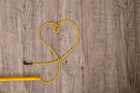 Heart of yellow headphones cable. Love listening music. Socket jack lying on wooden rustic background.の写真素材