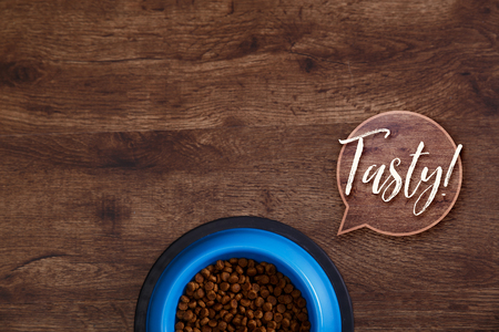 Bowl of dry kibble dog food. Healthy pets feed. Tasty speech bubble. Blue plate on wooden rustic background.の写真素材