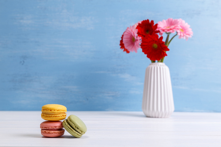 Macaroon cakes with Gerbera flowers. Different types of macaron. Colorful almond cookies. Blue wooden rustic background.の写真素材