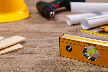 Helmet, screwdriver and tape measure. Paper plans and knife. Wooden planks and building level.