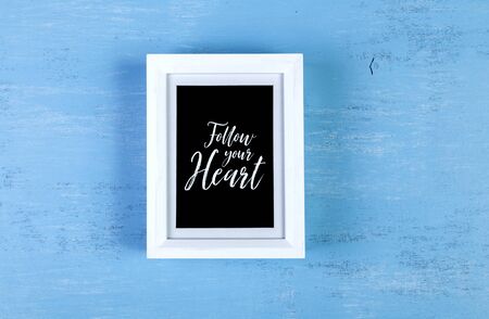 Blank photo frame on blue wood background. Follow your heart text. Painted scraped wooden board. Grunge plywood texture or pattern.の写真素材