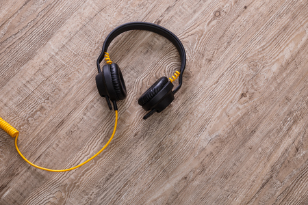 Headphones with yellow cable. Modern device for listening music. Sound earphones lying on wooden rustic background.の写真素材