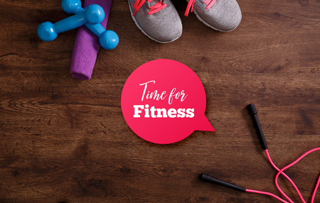 Fitness gym equipment. Sneakers, dumbbells with towel and skipping rope. Time for fitness speech bubble. Grunge rustic wood background.の写真素材