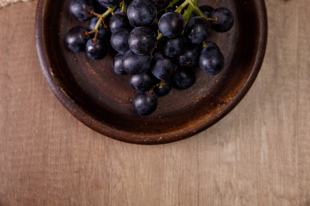 Dark grapes bunch. Ripe grape fruit on rustic plate. On wooden background.の写真素材