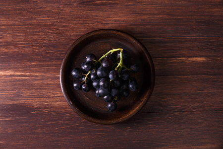 Dark grapes bunch. Ripe grape fruit on rustic plate. On wooden background.の写真素材