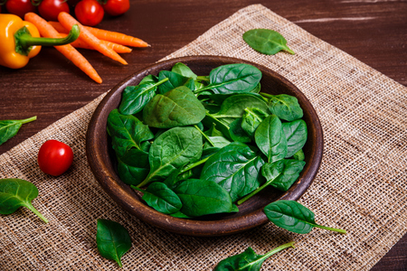 Spinach leaves in bowl. Carrot, pepper and cherry tomatoes. Raw fresh vegetable. Fresh natural plant leaf. Organic bio food on rustic wooden table.の写真素材