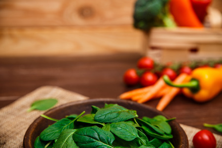 Spinach leaves in bowl. Carrot, pepper and cherry tomatoes. Raw fresh vegetable. Fresh natural plant leaf. Organic food on wooden table.の写真素材