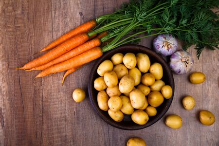 Potatoes in plate. Carrot, garlic and raw new potato. Fresh natural vegetables. Organic bio food on rustic wooden table.の写真素材