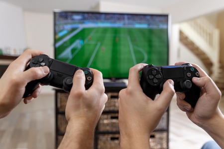 People playing video game. Hands holding console controller. Football or soccer game on the...