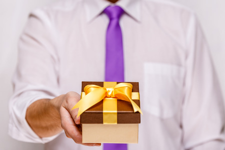 Male hand holding a gift box. Present wrapped with ribbon and bow. Christmas or birthday package. Man in white shirt and necktie.の写真素材