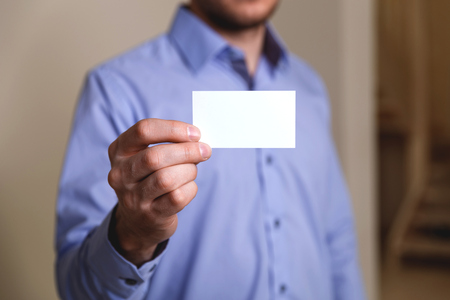 Manager holding visit card. Man showing blank business card. Person in blue shirt. Mock up design.の写真素材