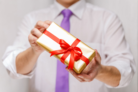 Male hands holding a gift box. Present wrapped with ribbon and bow. Christmas or birthday package. Man in white shirt and necktie.の写真素材