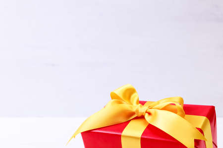 Gift box with yellow bow. Present wrapped with ribbon. Christmas or birthday red package. On white wooden table.の写真素材