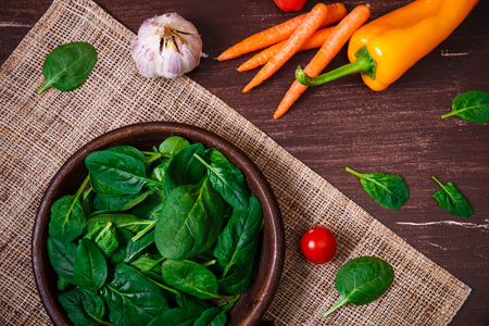 Spinach leaves in bowl. Carrot, pepper and cherry tomatoes. Garlic and brocoli. Raw fresh vegetable. Fresh natural plant leaf. Organic food on wooden table.の写真素材
