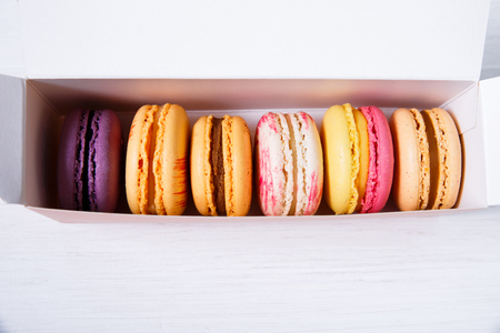Macaroon cakes. Colored almond macaron cookies. Delivery box. Different flavors. On white wooden rustic background.の写真素材