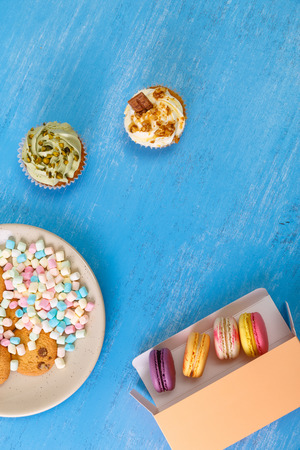 Macaroon cakes. Colored marshmallows. Cupcakes and Almond macaron cookies. Delivery box. On blue wooden rustic background.の写真素材