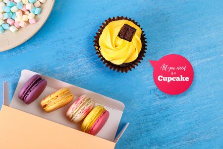 Macaroon cakes. Colored marshmallows. Cupcake and Almond macaron cookies. Delivery box. On blue wooden rustic background.の写真素材