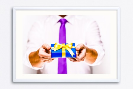 Male hands holding a gift box. Present wrapped with ribbon and bow. Christmas or birthday blue package. Man in white shirt and necktie. Wall frame poster with gift present box photo. Mockup template.の写真素材