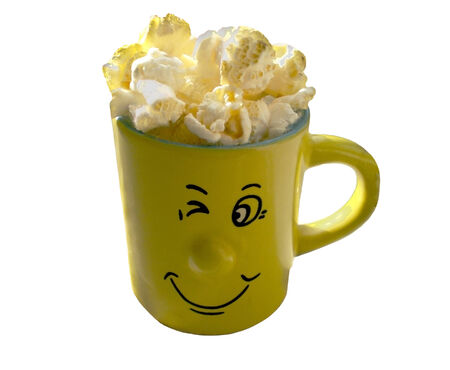 Cup of yellow colour with with a popcorn. On a cup the mug with a smile is drawn. The object is isolated on a white background.の写真素材