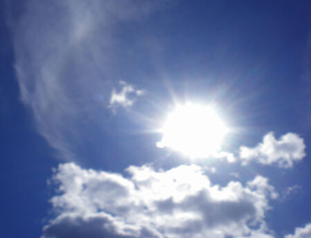 The bright sun is in the blue sky over white, air clouds.の写真素材
