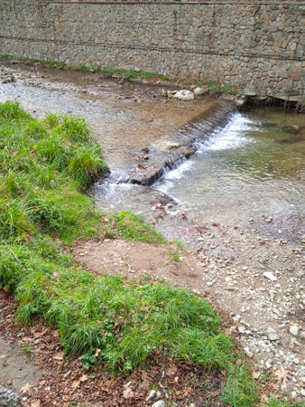 A small stream flows through a stone wall and grass in a small townの写真素材