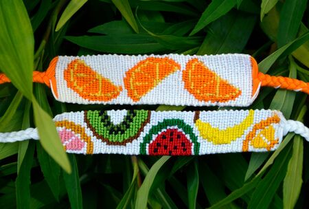 Two woven friendship bracelets handmade of threads with fruit patterns on green leaves backgroの写真素材