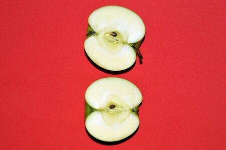 Two halves of a green juicy sliced ââapple on red backgroundの写真素材