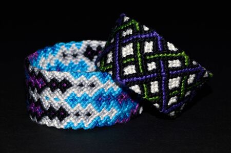 Colorful and multi-colored friendship bracelets handmade of embroidery bright thread with knots isolated on black backgroundの写真素材