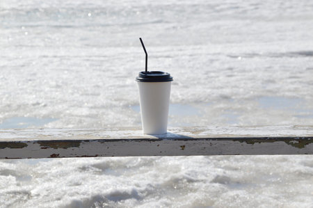 Coffee in the plastic cup standing on wooden bench against the background of melting sea in early...