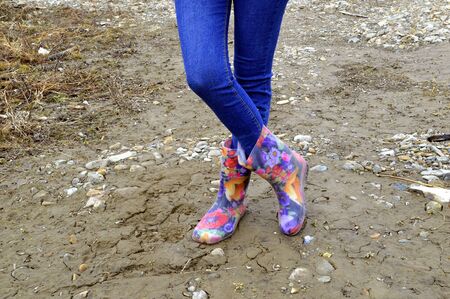 Women's legs in blue jeans and floral rubber boots on dirty soilの写真素材