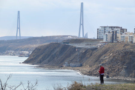 Vladivostok,Primorsky Krai, Russia - April 23, 2020:  Isolation and quarantine time, a man in bright red jacket standing on deserted cliff of bay of Patroclus (Patrokl)のeditorial素材