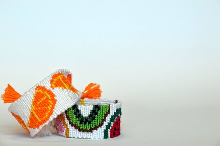 Handmade friendship bracelet with fruit pattern under bracelet with orange fruit pattern on gradient (blue,white,gray) background. Copy spaceの写真素材