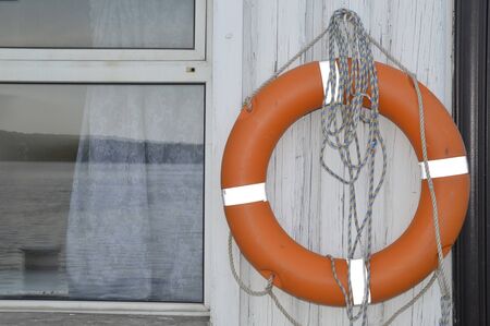 Orange life buoy hanging next to a window with a reflection of the sea.の写真素材