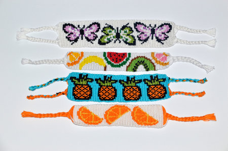 Woven friendship bracelets with alpha pattern fruit and butterflies handmade of thread on white backgroundの写真素材