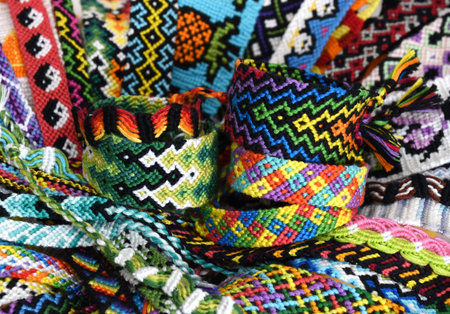 Tied woven DIY friendship bracelets on background of many multi-colored friendship bracelets...