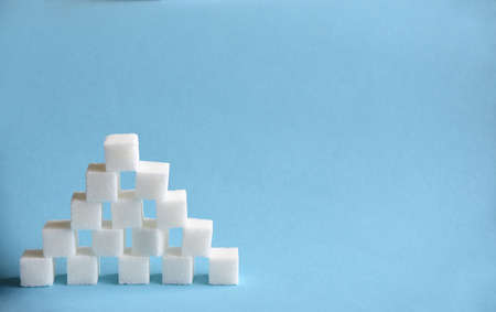 Pyramid made from cubes of refined white sugar on blue background. Copy spaceの写真素材