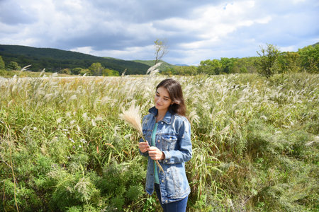 Young smiling woman holding bouquet of Miscanthus sinensis (Chinese silver grass) in her hands and...
