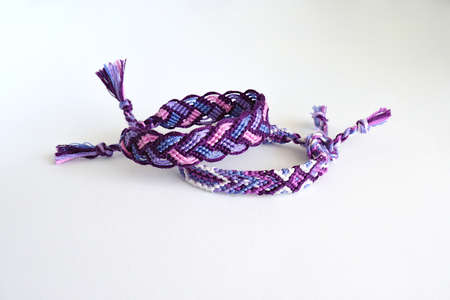 Selective focus of two purple woven DIY friendship bracelets handmade of embroidery bright thread with knots on white backgroundの写真素材
