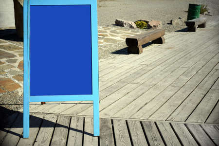 Blue blank advertising board on city street against wooden path with benches near caffee.の写真素材