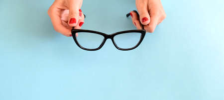 Female hands with red nail polish holding black glasses for eye vision with frame Cat's eye on a blue background. Copy spaceの写真素材