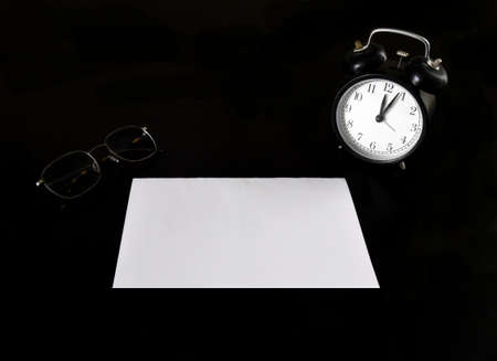 Black alarm clock with empty blank sheet of paper on a black table next to the glasses. business conceptの写真素材