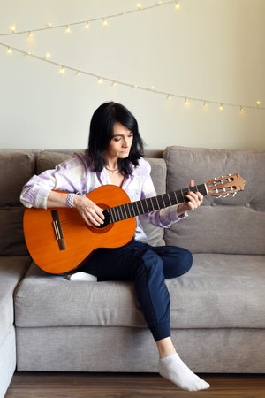 45 y.o. Russian woman playing guitar, sitting on a sofa at home.の写真素材