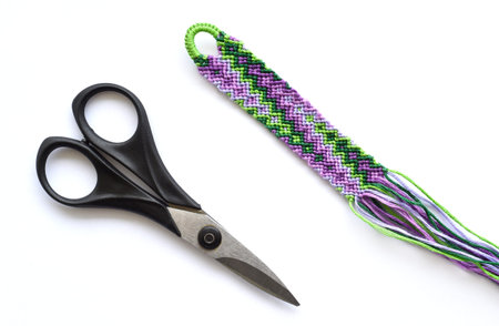 Unfinished woven DIY friendship bracelet with geyser pattern next to scissors on white background....